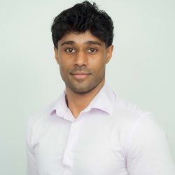 Dr SJ Siva Headshot, wearing white button up standing against blank white wall