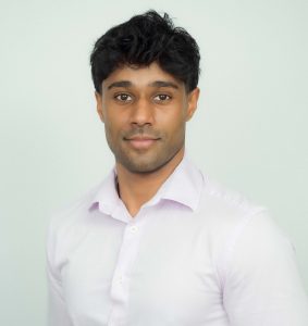 Dr SJ Siva Headshot, wearing white button up standing against blank white wall